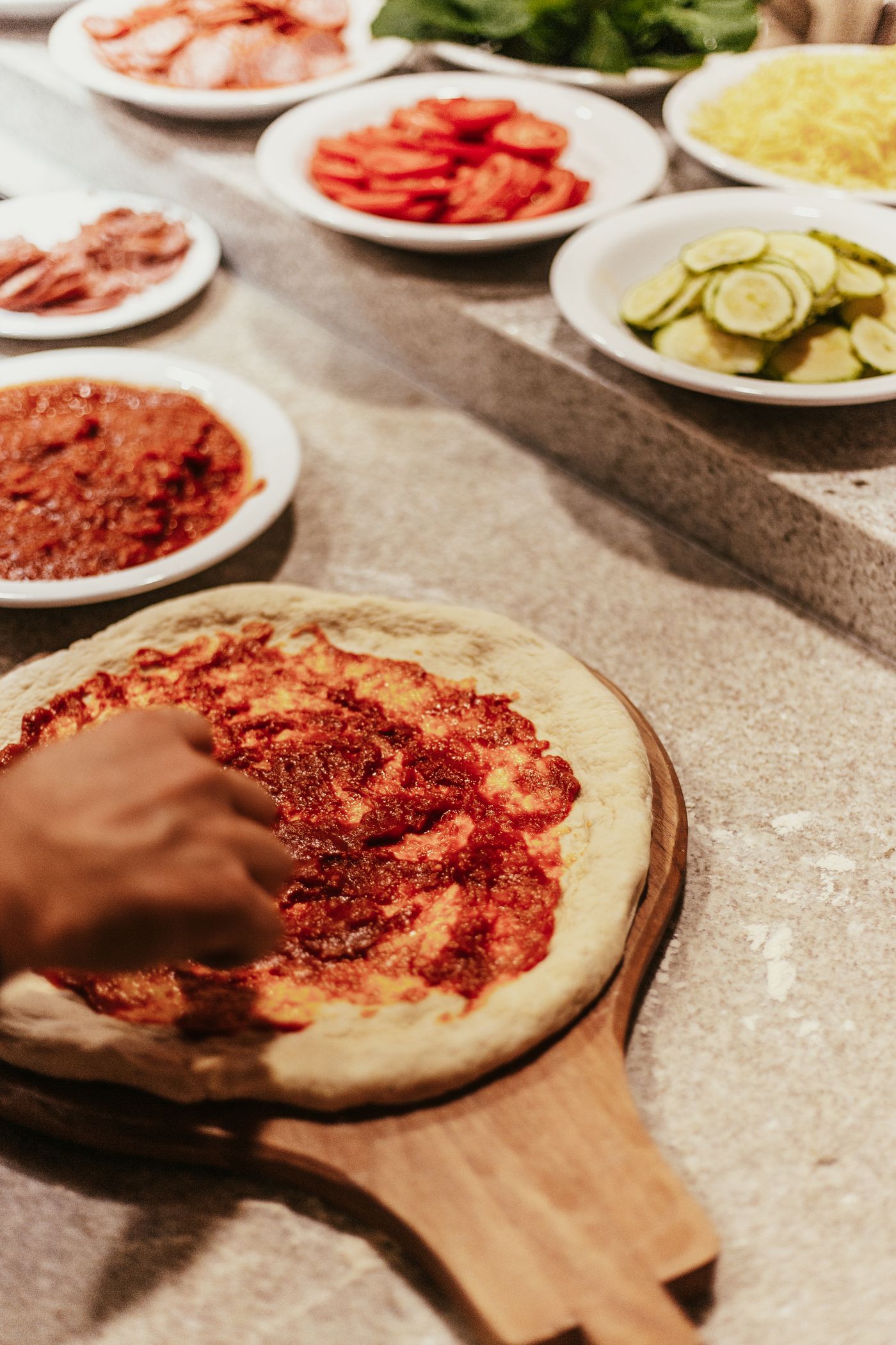 Préparation d’une pizza : la sauce tomate est étalée sur la pâte